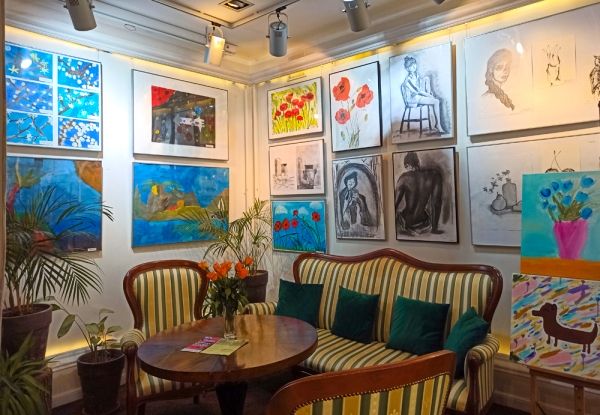 Wnętrze kawiarni CieKawa, przy okrągłym stole sofa i dwa fotele, obrazy na ścianach